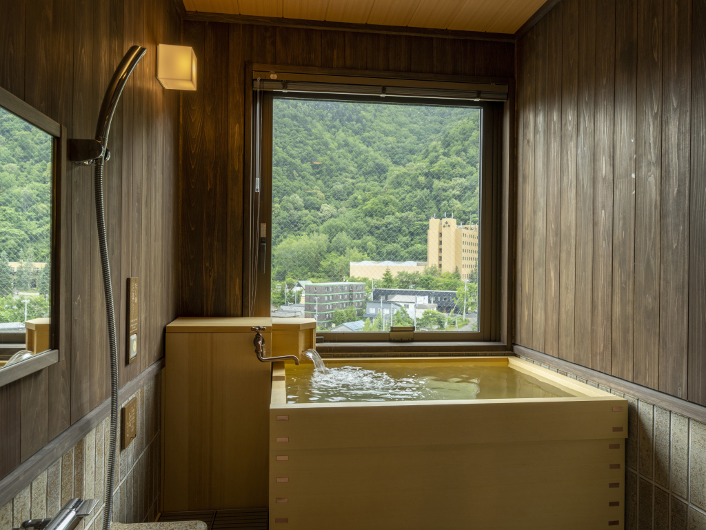 【天然温泉客室檜風呂（国道側）】窓から移ろう景色を眺めながら、気の向くままに何度でも湯浴みをお愉しみいただけます。